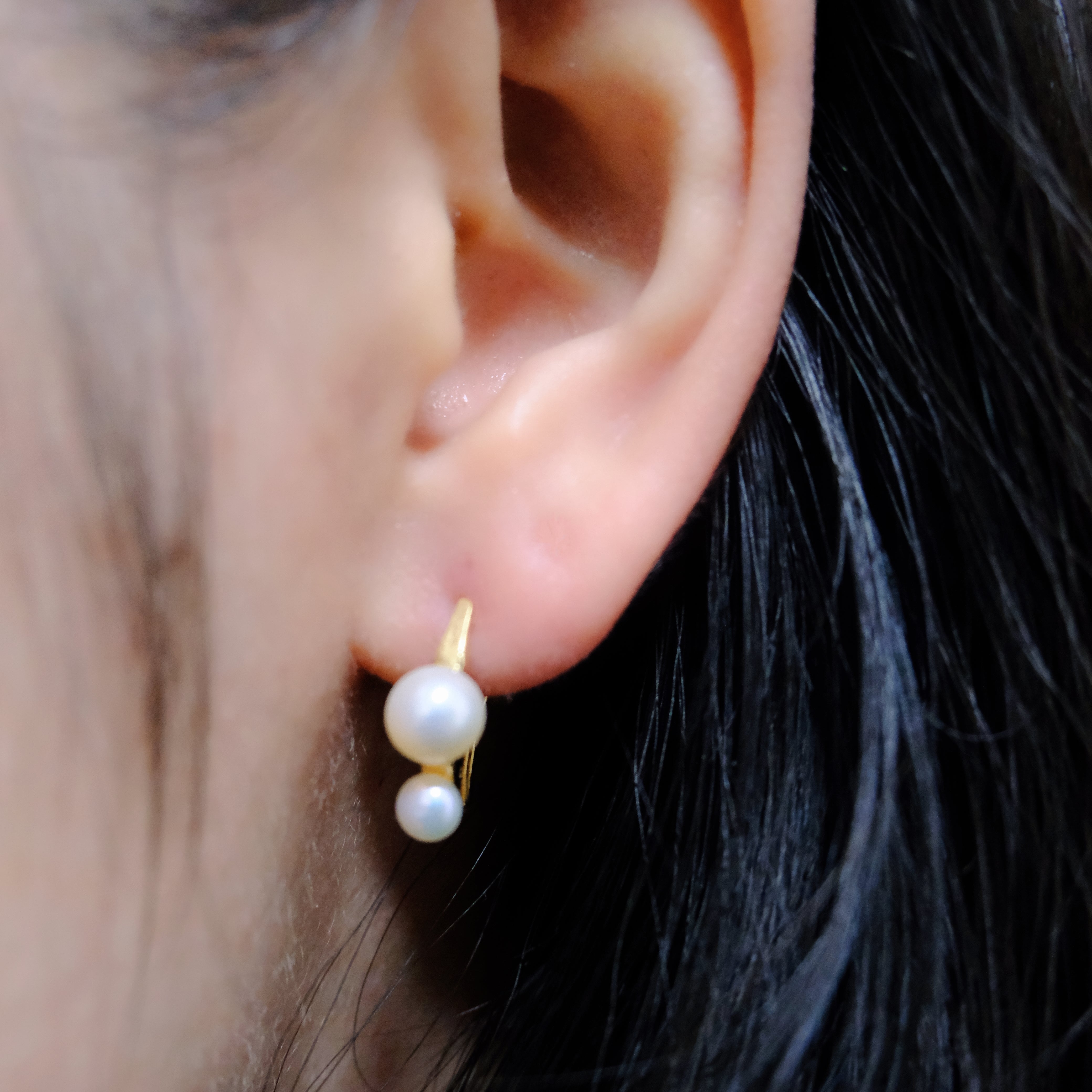 Gold-plated freshwater pearl stud earrings with curved hooks on an ear.