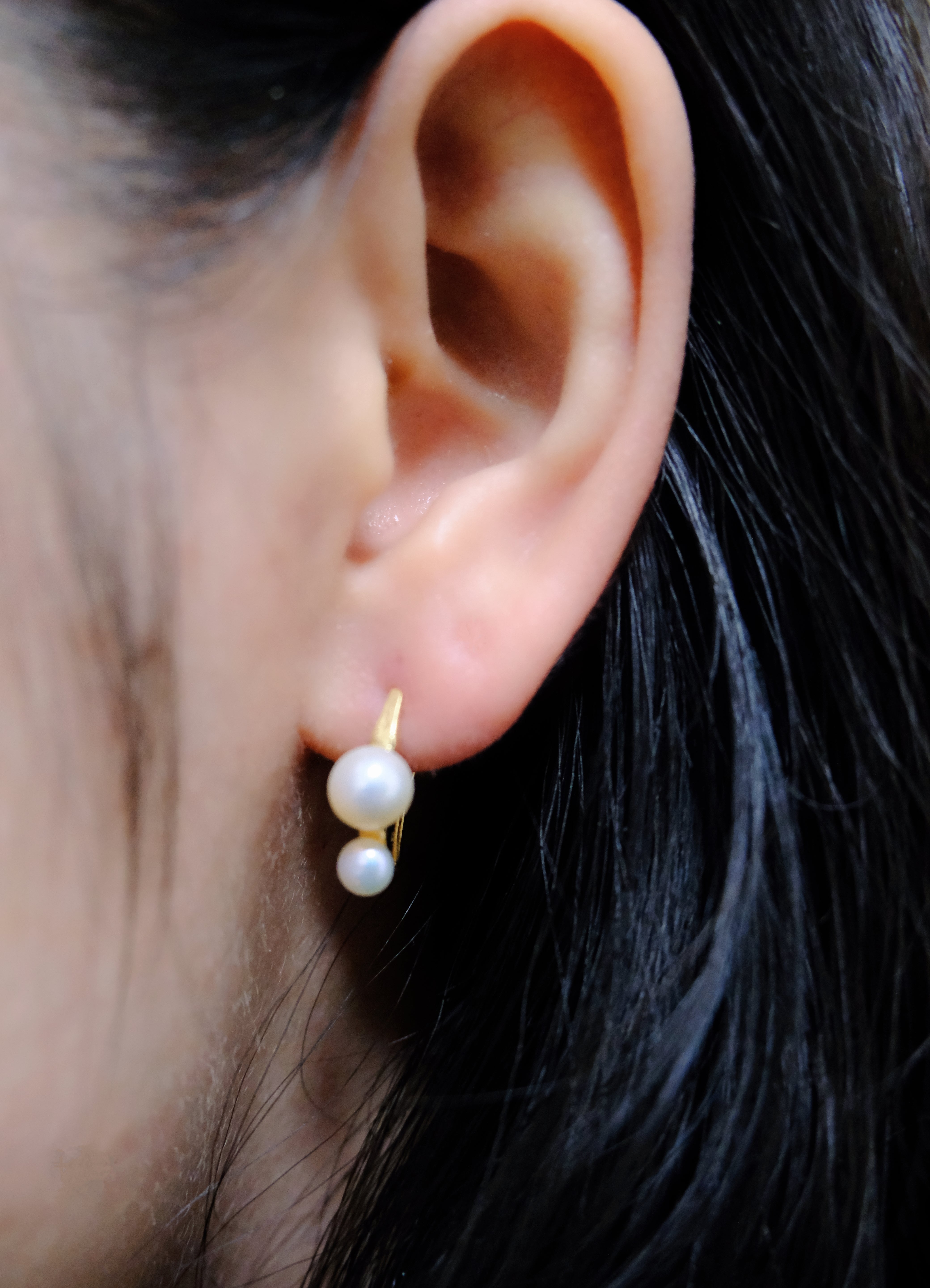 Gold-plated freshwater pearl stud earrings with curved hooks on an ear.