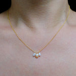 A gold chain necklace with three dangling freshwater pearls in white and peach tones.