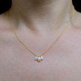 A gold chain necklace with three dangling freshwater pearls in white and peach tones.