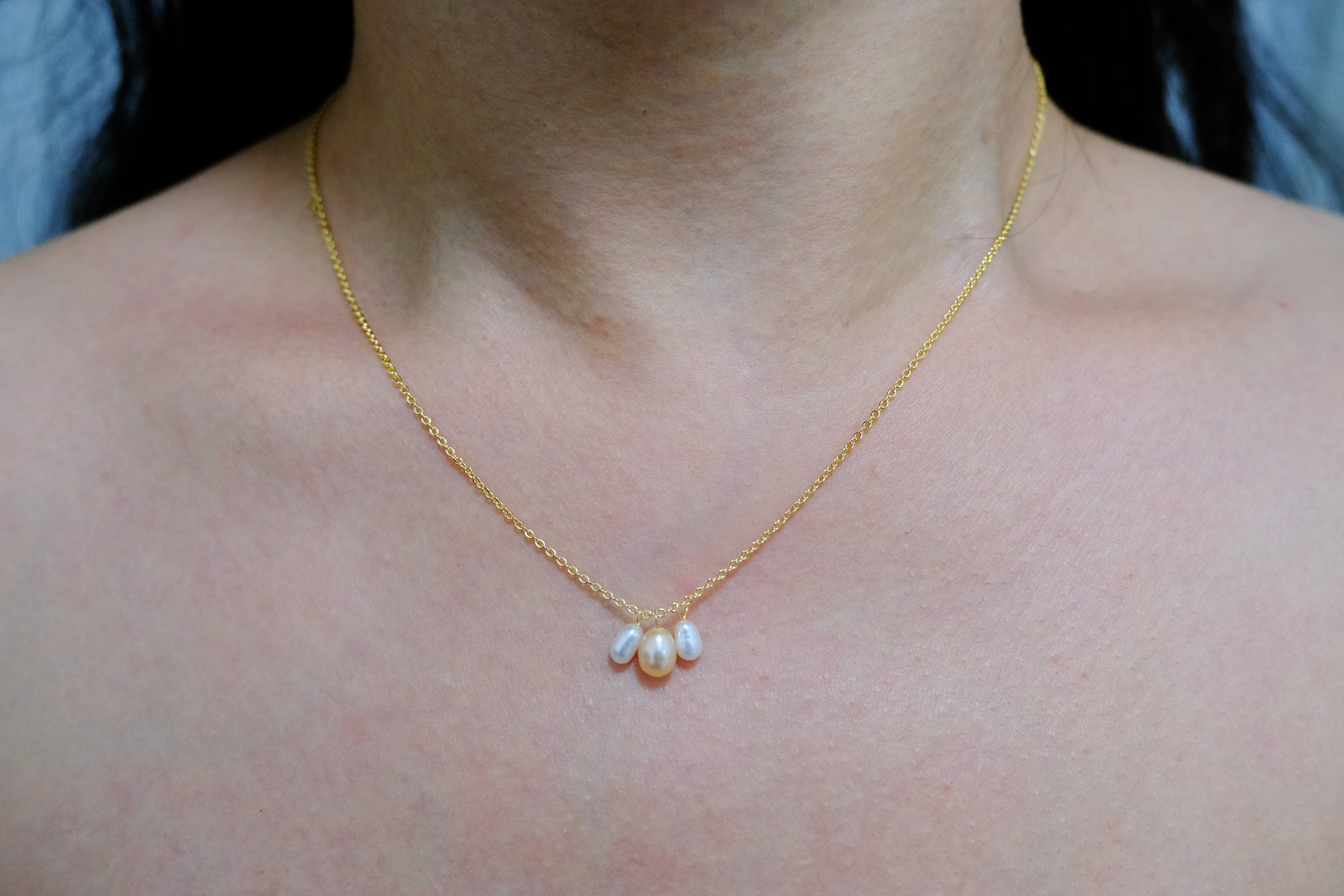 A gold chain necklace with three dangling freshwater pearls in white and peach tones.