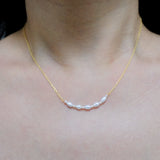 A woman wears a gold chain necklace with five freshwater pearls across her collarbone.