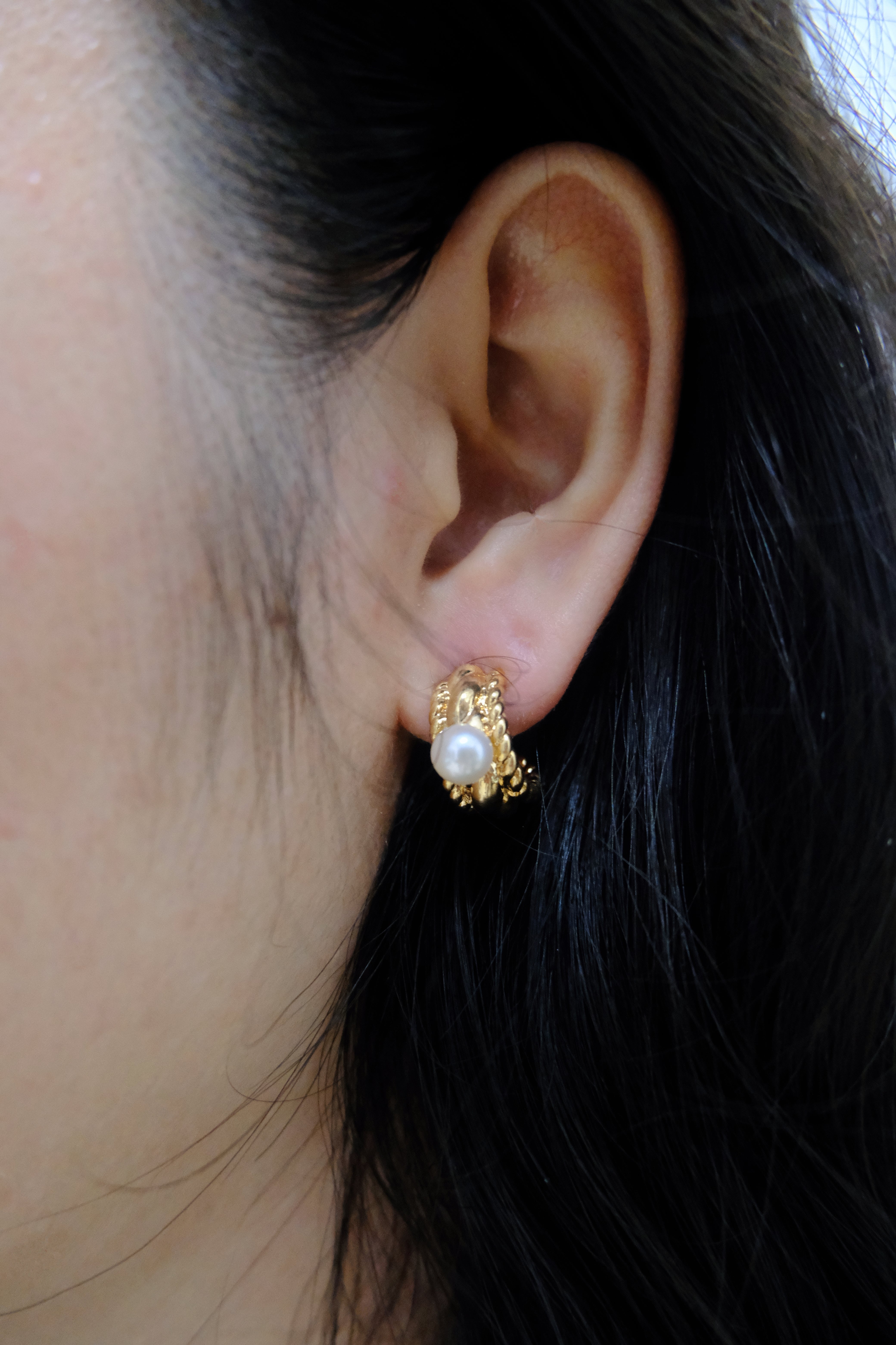 A close-up image of a woman's ear wearing a gold-plated pearl huggie hoop earring.