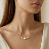 A model wears the Caellia 14K gold necklace featuring a central freshwater pearl and smaller beads.