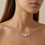 A woman wears a Caellia 14K gold chain necklace featuring a row of small freshwater pearls.