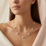A woman wears a Caellia dainty 14K gold chain necklace featuring spaced freshwater pearls.
