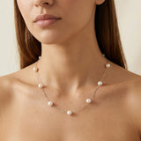 A woman wears a Caellia dainty 14K gold chain necklace featuring spaced freshwater pearls.