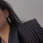 Three pearl drop earrings on a person wearing a pinstripe blazer.