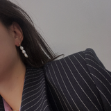Three pearl drop earrings on a person wearing a pinstripe blazer.