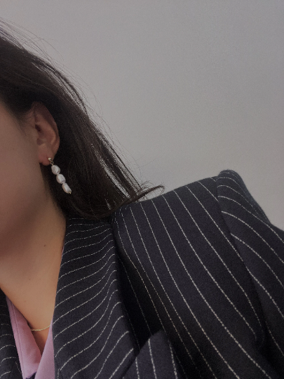 Three pearl drop earrings on a person wearing a pinstripe blazer.