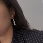 Three pearl drop earrings on a woman wearing a pinstripe blazer.