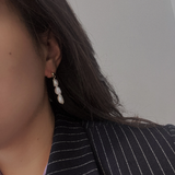 Three pearl drop earrings on a woman wearing a pinstripe blazer.