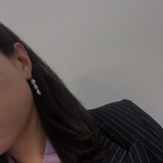 Three pearl drop earrings on a person's ear, with a pinstripe blazer.