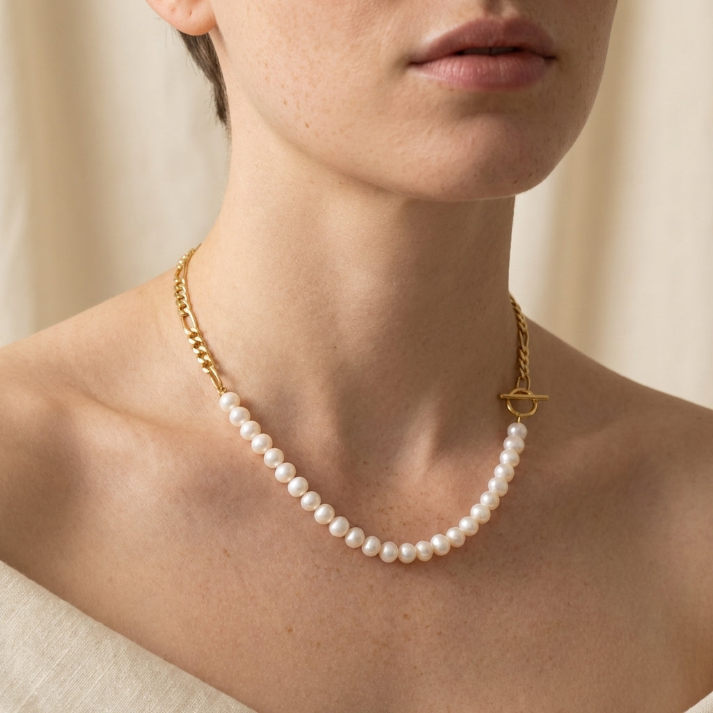 A person wears a Caellia 14K gold plated necklace featuring freshwater pearls and a toggle clasp.