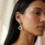 A model wears Caellia 14K gold hoop earrings featuring a dangling circular freshwater pearl charm.