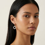 A model wears Caellia 14K gold hoop earrings featuring a dangling circular freshwater pearl charm.