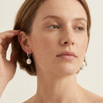 A model wears Caellia sterling silver hoop earrings featuring dangling freshwater pearls.