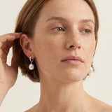 A model wears Caellia sterling silver hoop earrings featuring dangling freshwater pearls.