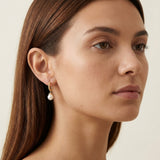 A model wears Caellia 14K gold half hoop earrings featuring a dangling white freshwater pearl.