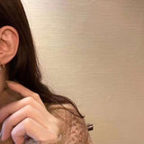 A person wears a Caellia 14K gold music note earring featuring a freshwater pearl.