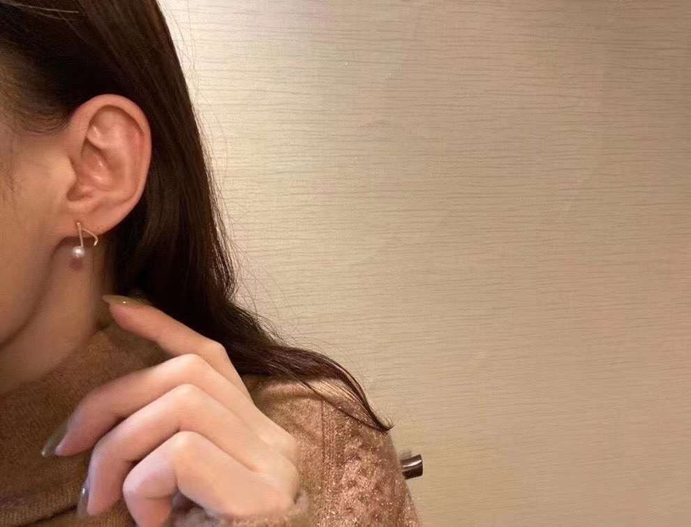 A person wears a Caellia 14K gold music note earring featuring a freshwater pearl.