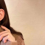 A person wears Caellia 14K gold music note earrings featuring two freshwater pearls.