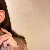 A person wears Caellia 14K gold music note earrings featuring two freshwater pearls.
