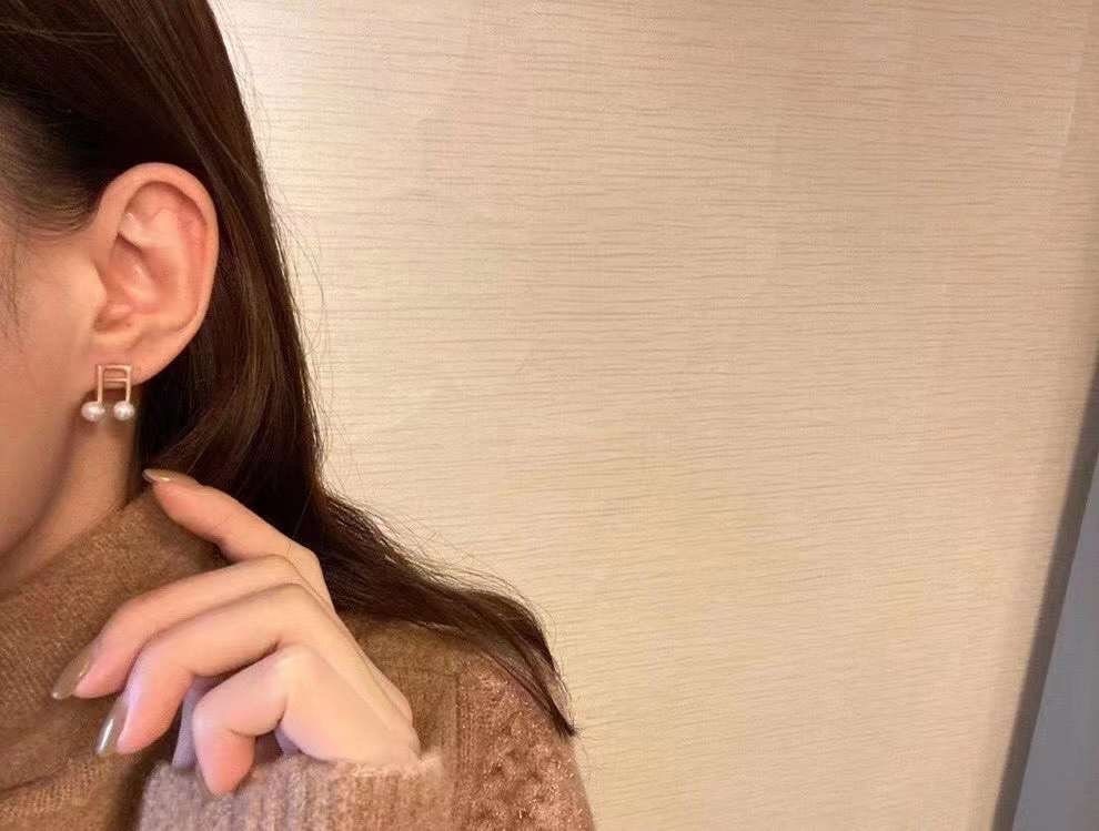 A person wears Caellia 14K gold music note earrings featuring two freshwater pearls.