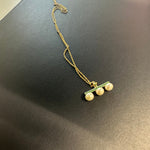 A gold-plated necklace features a green bar pendant with three pearls.