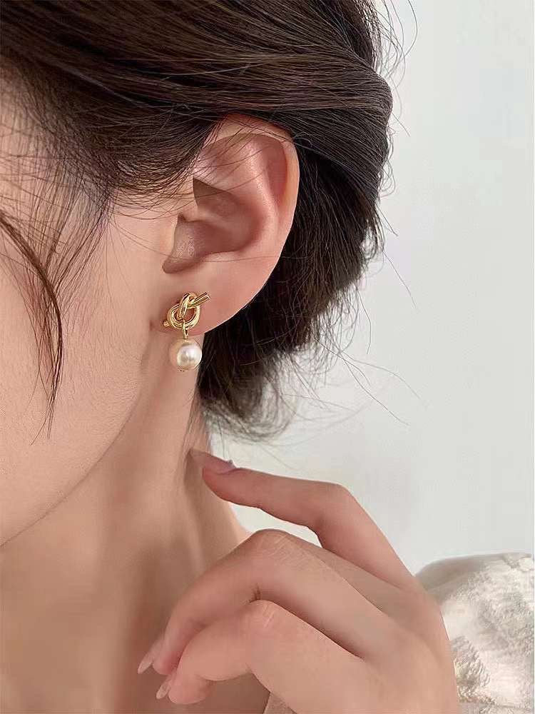 Caellia 14K gold knot earrings featuring a dangling freshwater pearl worn on an earlobe.