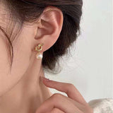 Caellia 14K gold knot earrings featuring a dangling freshwater pearl worn on an earlobe.
