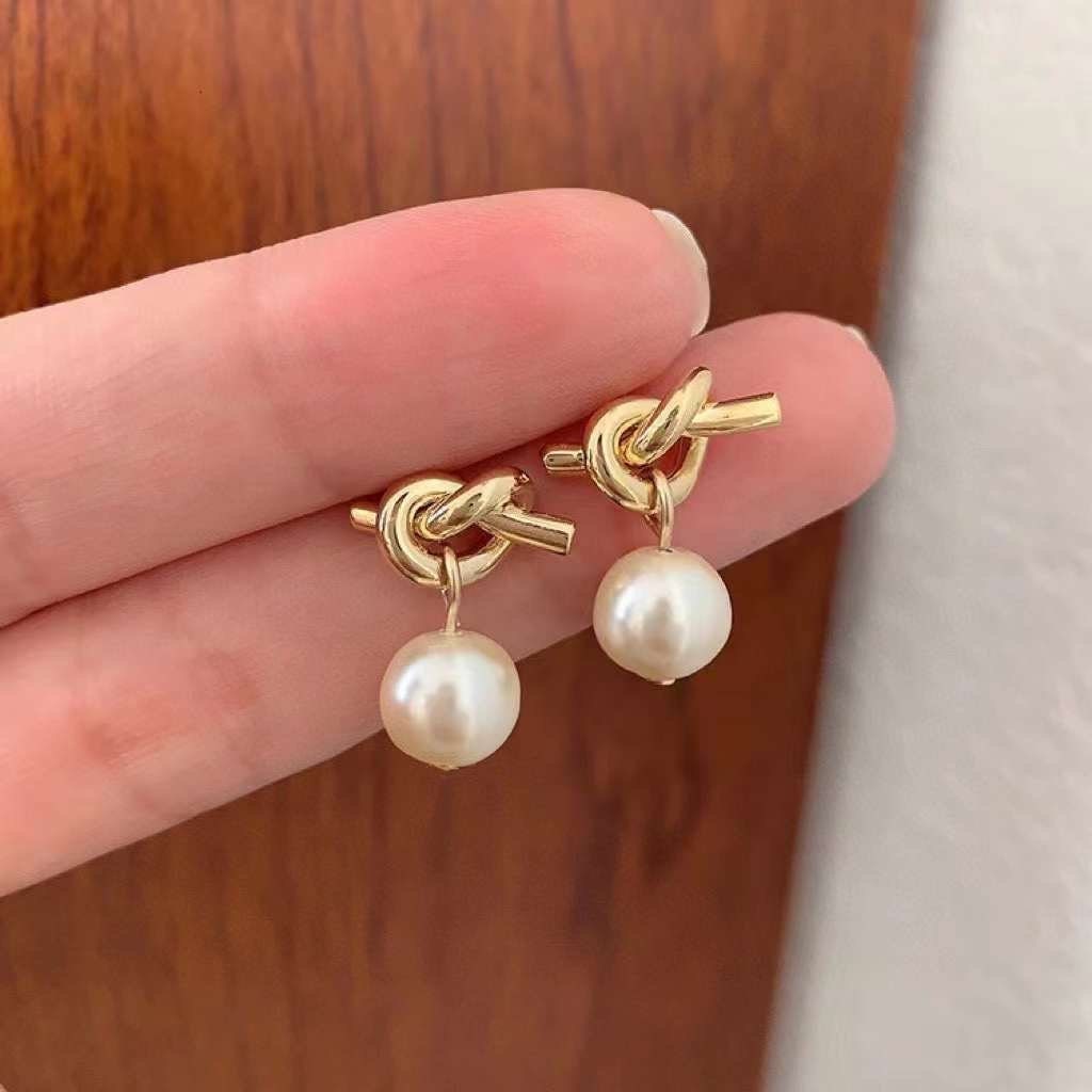 Caellia 14K gold knot earrings featuring a dangling freshwater pearl drop.