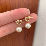 Caellia 14K gold knot earrings featuring a dangling freshwater pearl drop.