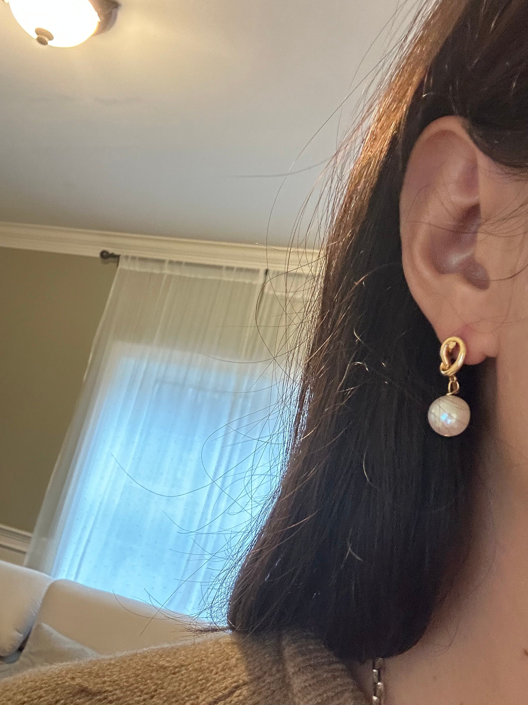 Casual close-up of a gold knot freshwater pearl drop earring worn