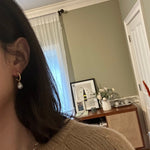 A person wearing CAELLIA 14k gold plated half hoop earrings with a round white pearl drop.