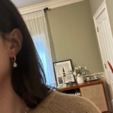 A person wearing CAELLIA 14k gold plated half hoop earrings with a round white pearl drop.