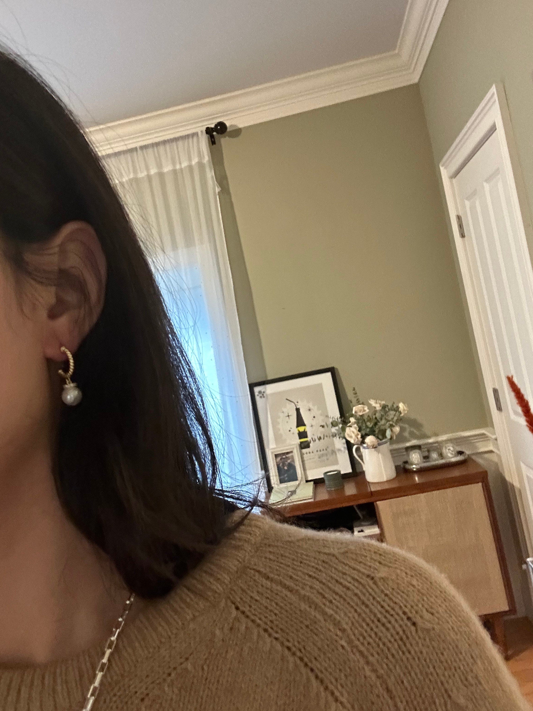 A person wearing CAELLIA 14k gold plated half hoop earrings with a round white pearl drop.