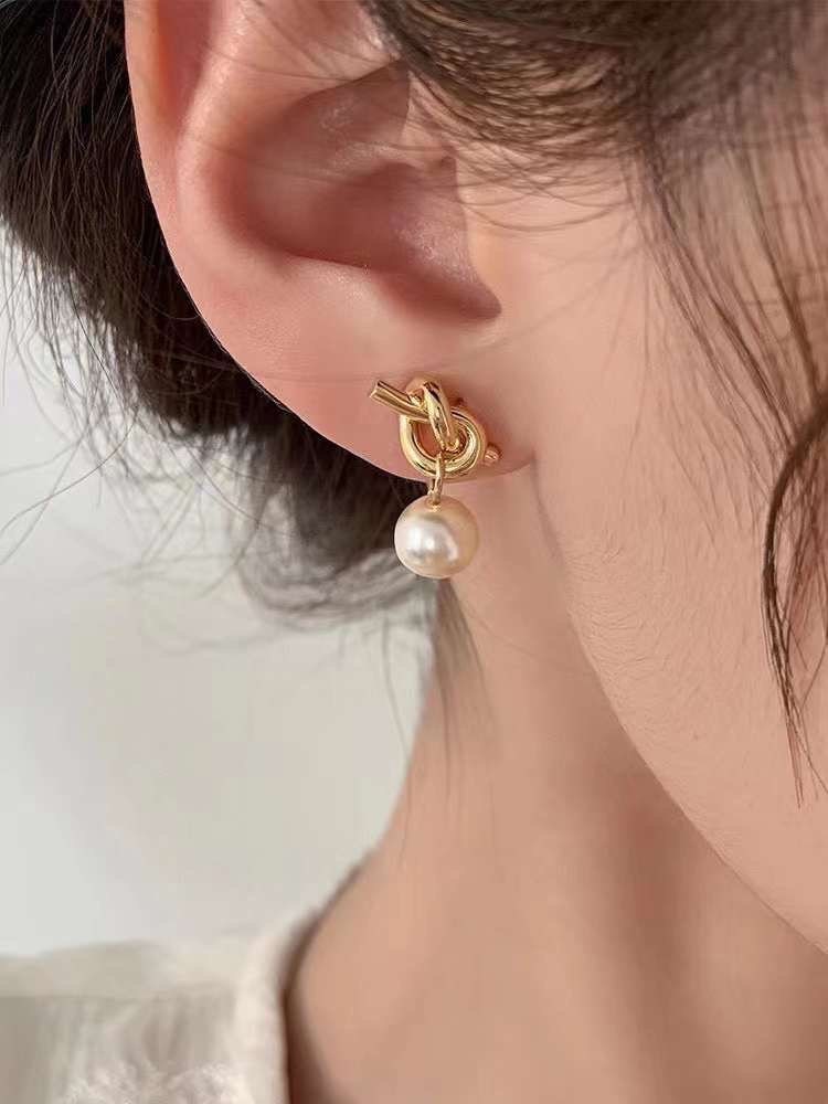 Caellia 14K gold knot earrings featuring a dangling freshwater pearl worn on an earlobe.