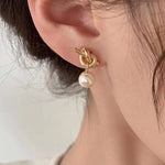 Caellia 14K gold knot earrings featuring a dangling freshwater pearl worn on an earlobe.