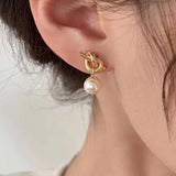 Caellia 14K gold knot earrings featuring a dangling freshwater pearl worn on an earlobe.
