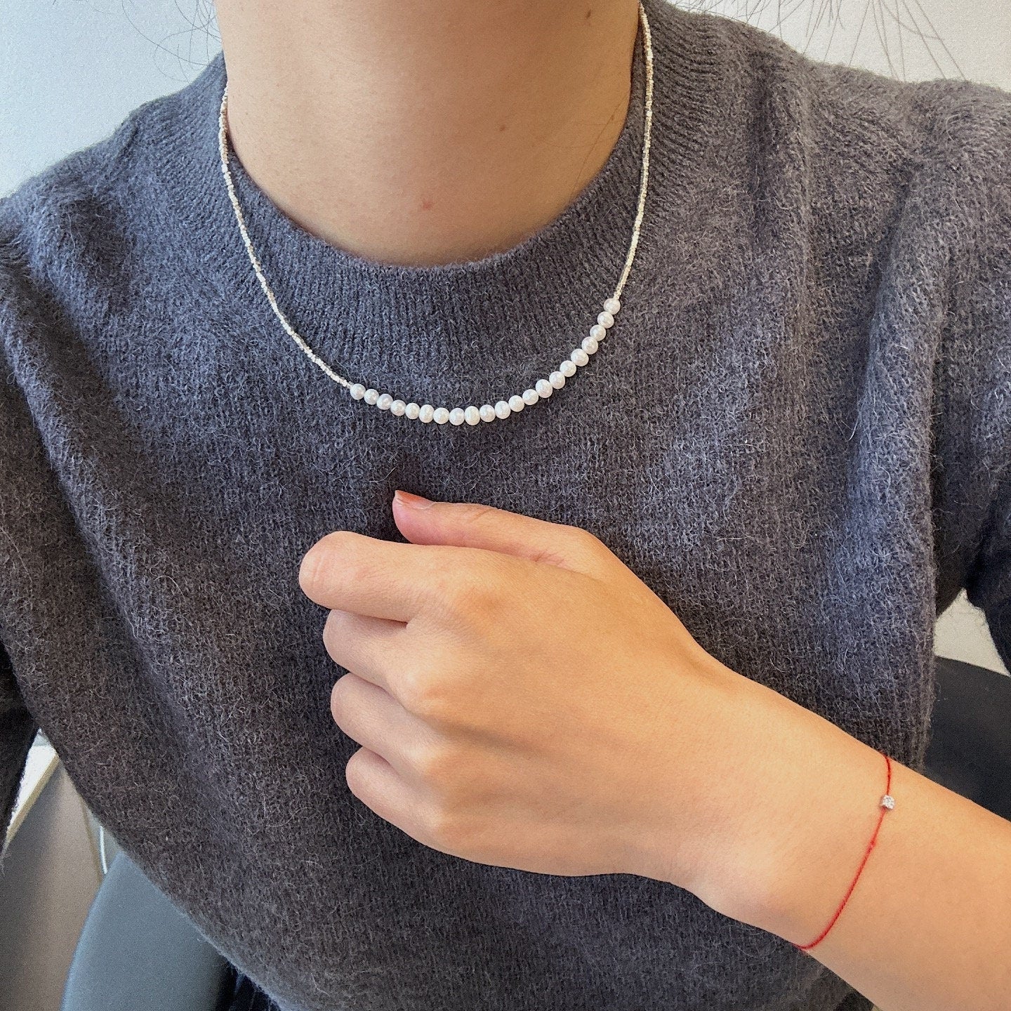 A CAELLIA minimalist freshwater pearl necklace worn with a grey sweater.