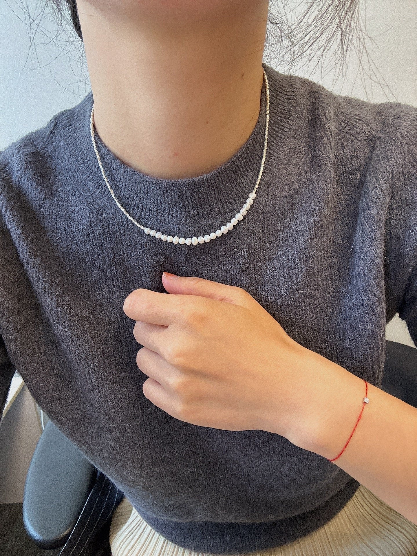 A CAELLIA minimalist freshwater pearl necklace worn with a grey sweater.