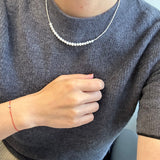 Small around bead pearl necklace with a red string bracelet on a person.
