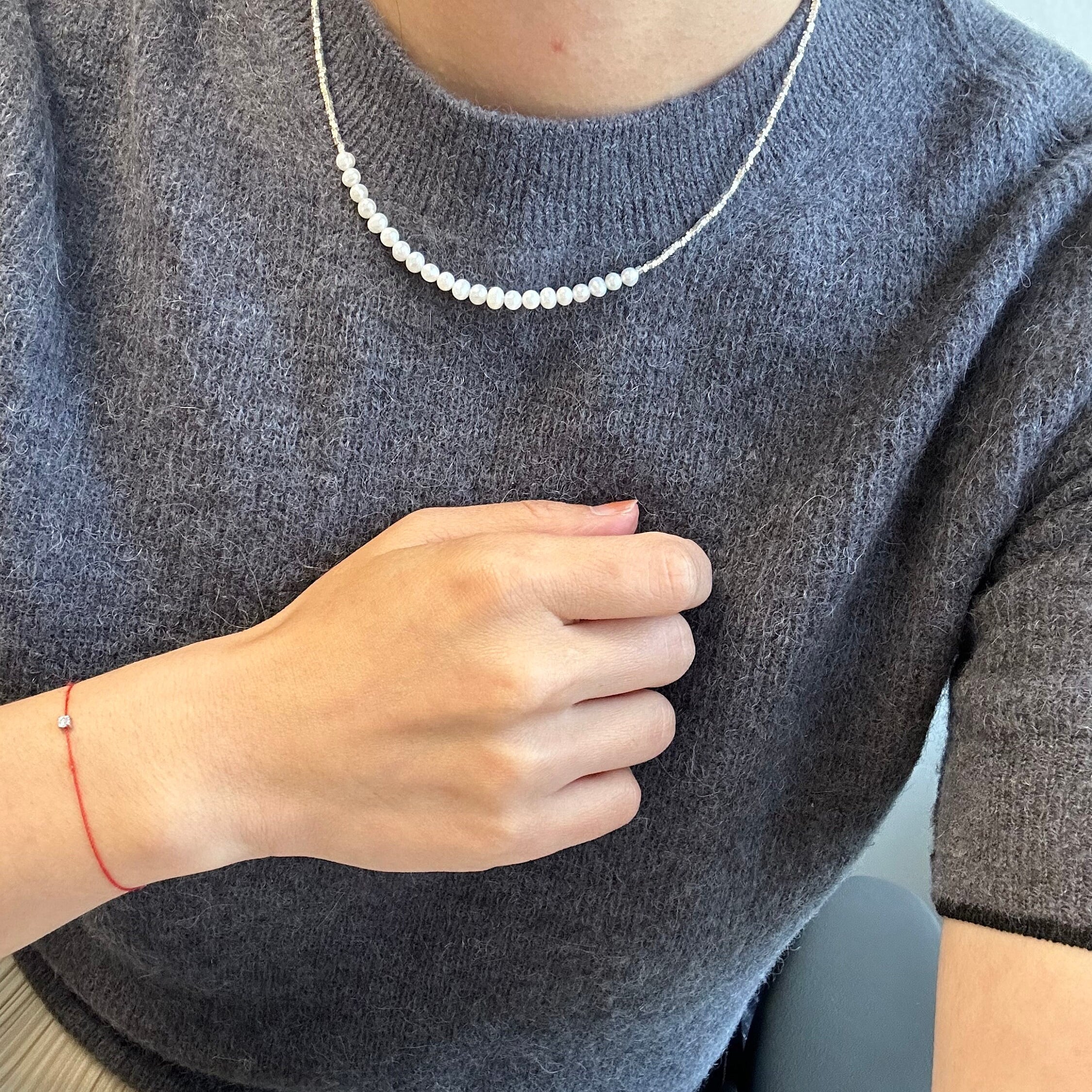 Small around bead pearl necklace with a red string bracelet on a person.