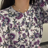 A woman wears a gold-plated pearl necklace with a white floral blouse.
