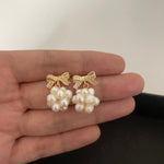 Caellia 14K gold bowknot earrings featuring clusters of freshwater pearls held in a hand.