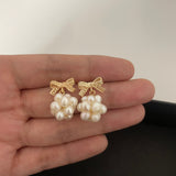 Caellia 14K gold bowknot earrings featuring clusters of freshwater pearls held in a hand.