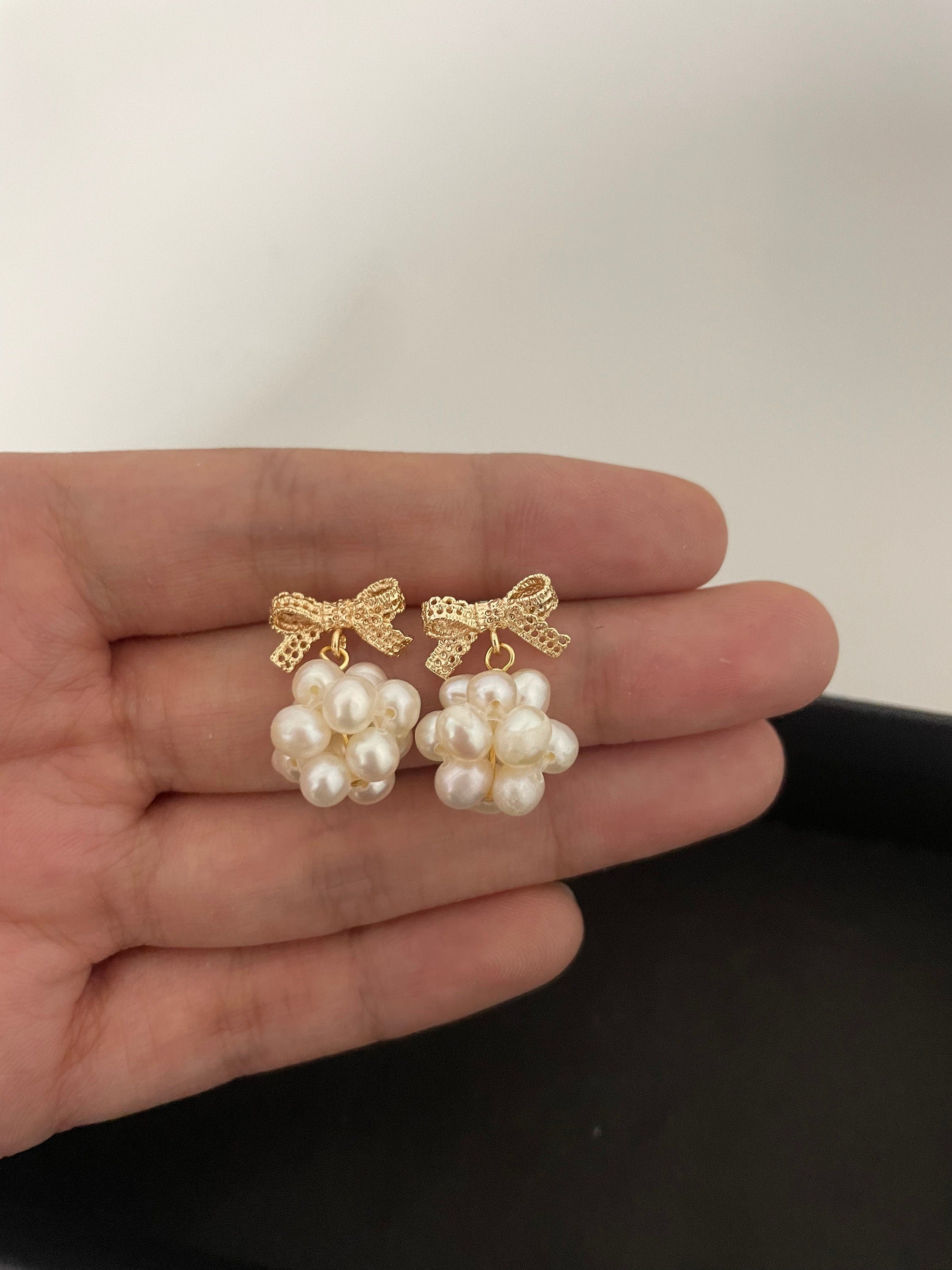 Caellia 14K gold bowknot earrings featuring clusters of freshwater pearls held in a hand.