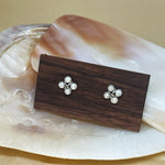 CAELLIA freshwater pearl rhomboid stud earrings displayed on a wooden block over a shell.