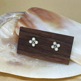 CAELLIA freshwater pearl rhomboid stud earrings displayed on a wooden block over a shell.